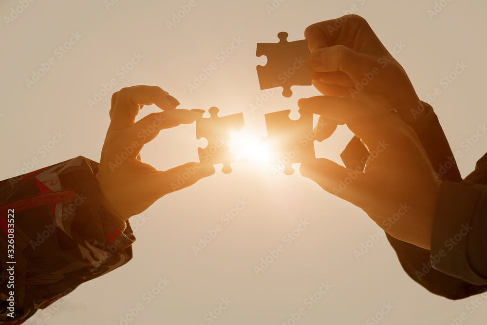 Three pieces of puzzles in the hands of a group of people on the background of the glare of the sun. The concept of teamwork, interaction.
