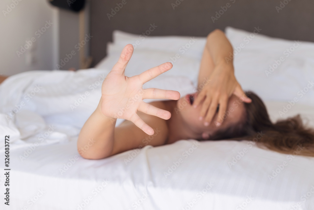 Young woman hides her surprised and indignant face from the camera lying on a bed in the bedroom and covered sheet