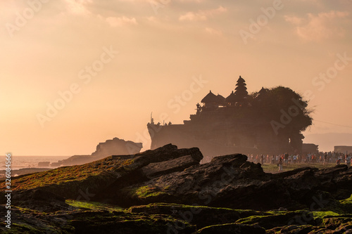 Ancient Tanah Lot temple with tourists on coastline in sunset