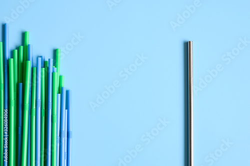 a pile of disposable plastic drinking straws and one reusable stainless steel metal drinking straw on a blue background