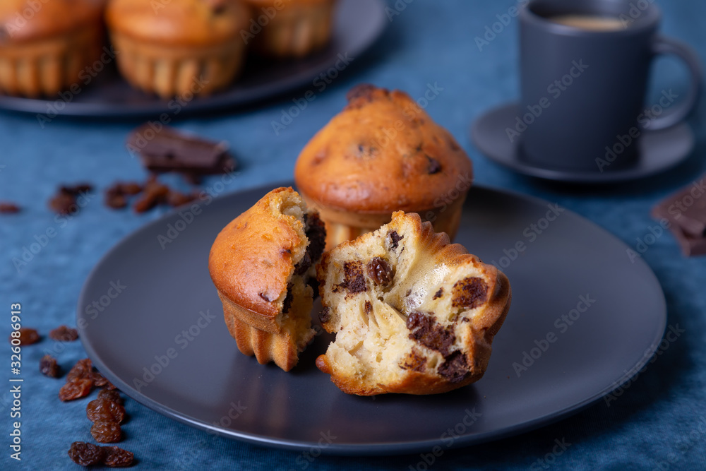 Muffins with chocolate and raisins. Homemade baking. In the background is a plate with muffins and a cup of coffee. Blue background. Close-up.
