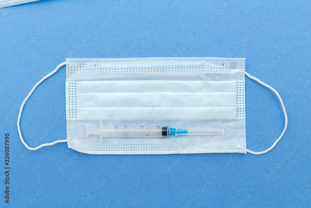 medical protective mask, syringe with copy space on a blue background. medical protective mask, syringe with copy space on a blue background.