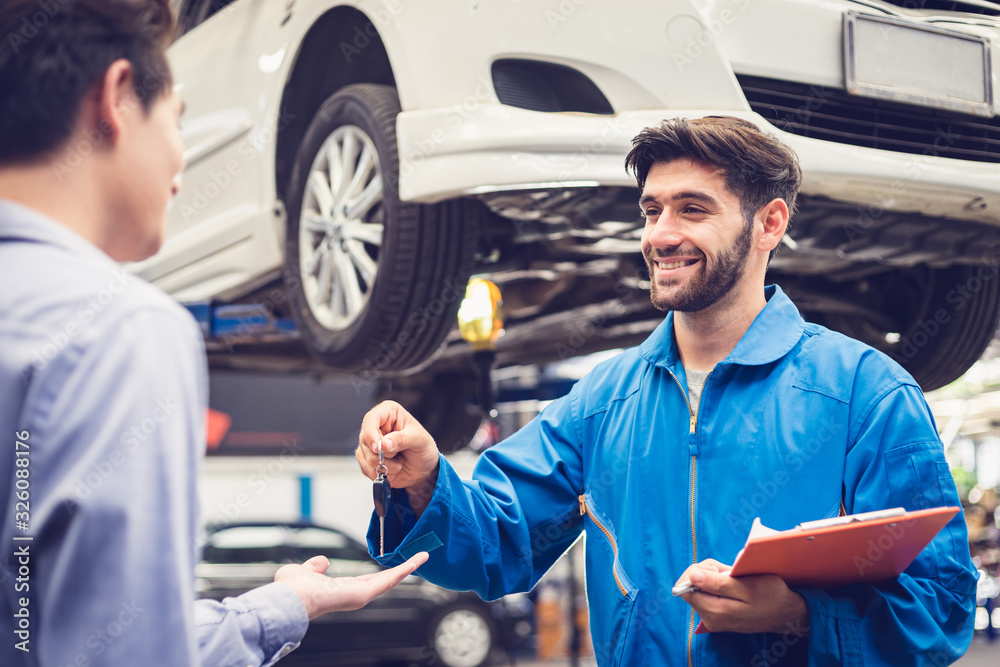 Mechanic holding clipboard giving the key back to car owner in the workshop garage. Car auto services concepts Mechanic holding clipboard giving the key back to car owner in the workshop garage. Car auto services concepts