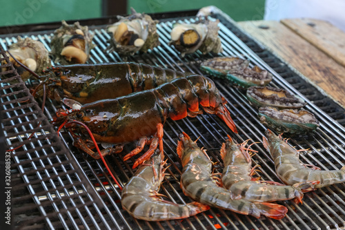 Lobster, rock lobster and mix seafood barbecue cokking on grill - seafood dinner party concept. photo