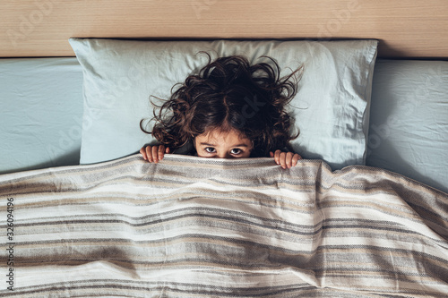 little girl covering her face with the bedspread photo