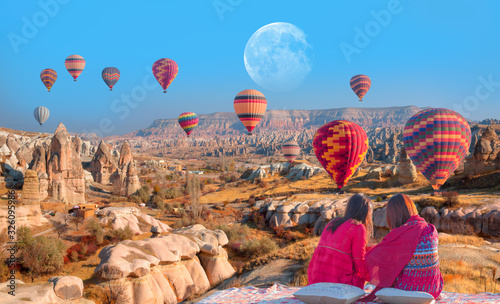 Hot air balloon flying over spectacular Cappadocia - Girls watching hot air balloon at the hill of Cappadocia "Elements of this image furnished by NASA