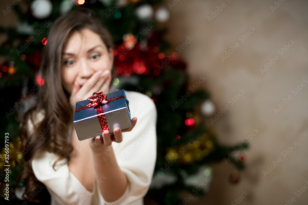 girl rejoices and is surprised at the gift that she holds in her hand against the background of the New Year tree girl rejoices and is surprised at the gift that she holds in her hand against the background of the New Year tree