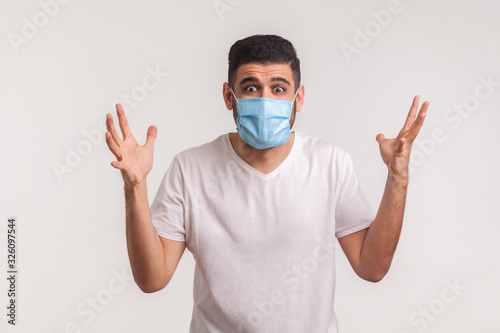 Panicking man in hygienic mask raising hands in fear, gesturing question what to do, afraid of sudden coronavirus outbreak, lack of knowledge about novel influenza 2019-nCoV. studio shot, isolated