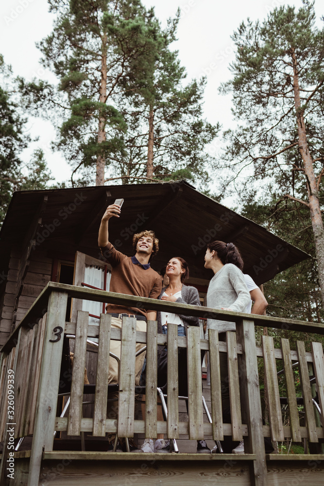 Smiling friends taking selfie with mobile phone while standing in porch Smiling friends taking selfie with mobile phone while standing in porch