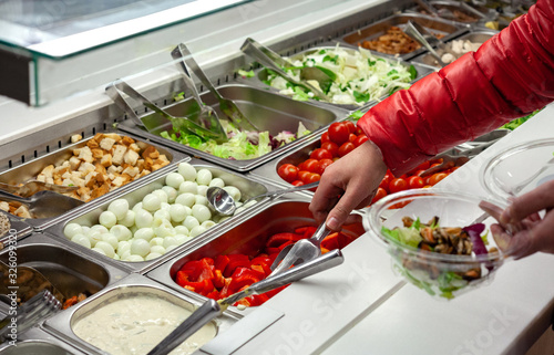 Bild auf Leinwand Fresh Salad bar counter with person's hands lifting vegetable into a salad bowl