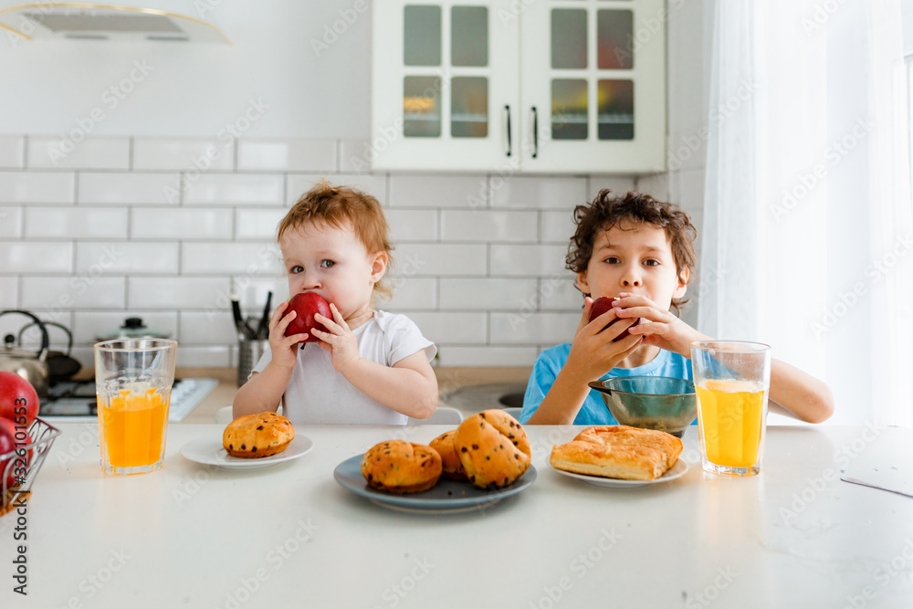 Happy children real brother and sister having breakfast with fruits in bright kitchen at the home Happy children real brother and sister having breakfast with fruits in bright kitchen at the home