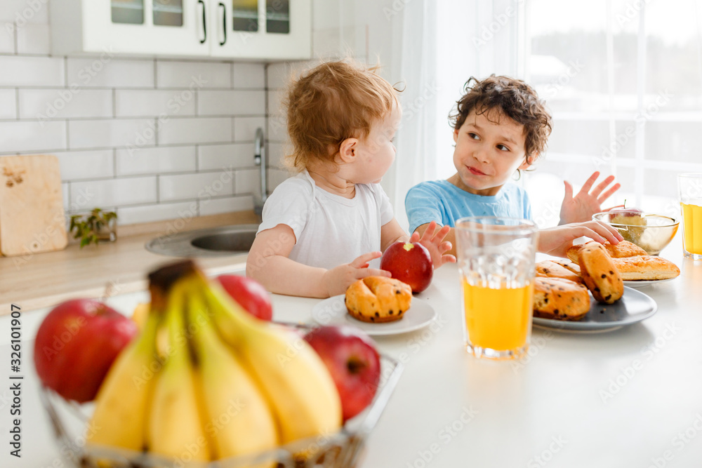 Happy children real brother and sister having breakfast with fruits in bright kitchen at the home