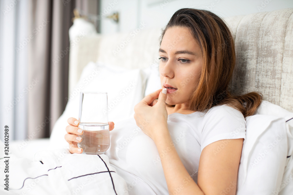 Ill woman taking a painkiller pill on a bed Ill woman taking a painkiller pill on a bed