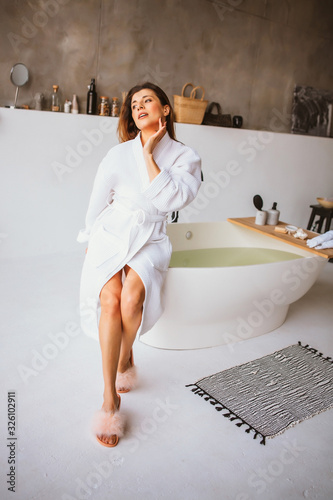 Beautiful woman relaxing in white bathrobe near bath photo