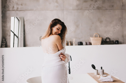 Beautiful woman relaxing in white bathrobe near bath photo