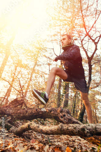 The concept of sports and cross-country running. A man in sports clothes jumps branches on the ground, doing a run. Forest in the background. Blurred action. View from the bottom. Sunlight © _KUBE_