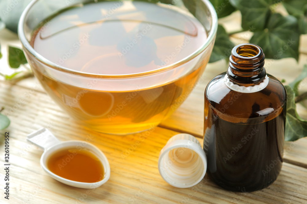 Ivy leaf and syrup in a bottle on a natural wooden table. Production of cough medicine with ivy extract. pharmaceutical industry Ivy leaf and syrup in a bottle on a natural wooden table. Production of cough medicine with ivy extract. pharmaceutical industry