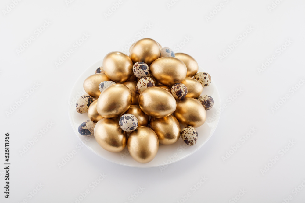 Golden eggs mixed with quail in a plate, on a white background. The concept of Easter, a symbol of the holiday, abundance and wealth. Golden eggs mixed with quail in a plate, on a white background. The concept of Easter, a symbol of the holiday, abundance and wealth.