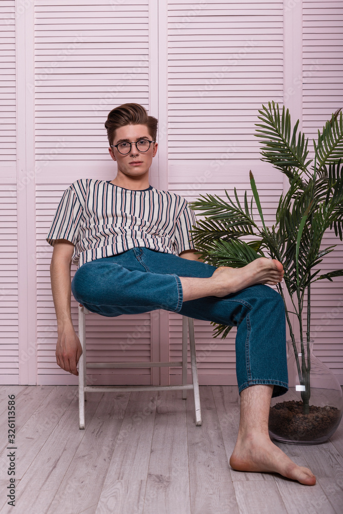 American stylish young man hipster in a fashionable striped T-shirt in jeans  with glasses sits