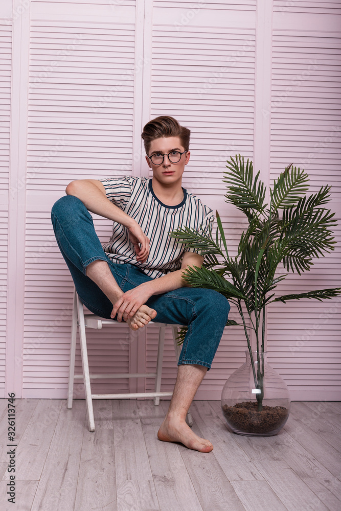 Sexy stylish young man hipster in a fashionable T-shirt in vintage glasses  sits on a