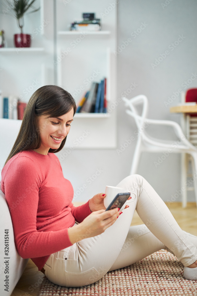 Young attractive smiling woman sitting on the floor at home, using smart phone and relaxing. Young attractive smiling woman sitting on the floor at home, using smart phone and relaxing.