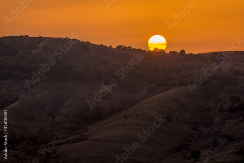 Beautiful landscape of a big setting sun over the silhouette of the mountains, Vulcanii noroiosi, Berca, Paclele, Romania