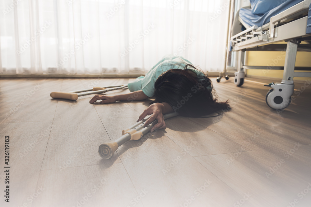 The female patient lay dawn on the floor Near the patient's bed, while holding the armpit crutches, to people and health care concept.