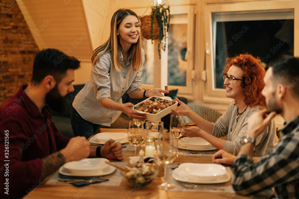 Happy woman serving dinner to her friends at dining table.
