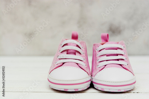Close up pink baby girl sneakers, sport shoes close up on gray background. Newbord, motherhood, pregnancy concept with copy space.