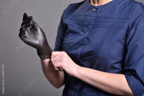 Young woman puts on black latex gloves before procedures. Close-up