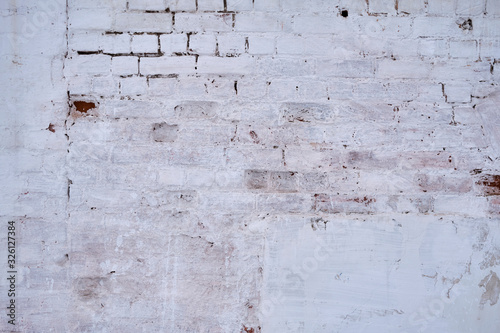 Background. An old, dirty, white brick wall with peeled paint and peeled plaster.