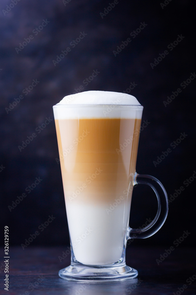 Latte macchiato in a tall glass on a dark background. Cafe latte layered with milk in a high drinking glass. Minimalism. Сopy space
