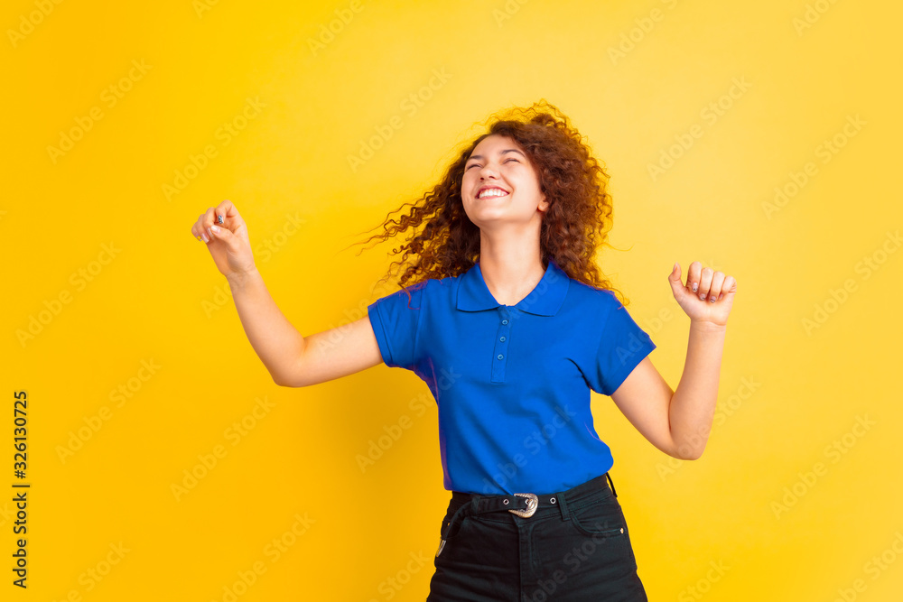 Dancing with flying hair. Caucasian teen's girl portrait on yellow studio background. Beautiful female curly model. Concept of human emotions, facial expression, sales, ad, education. Copyspace. Dancing with flying hair. Caucasian teen's girl portrait on yellow studio background. Beautiful female curly model. Concept of human emotions, facial expression, sales, ad, education. Copyspace.