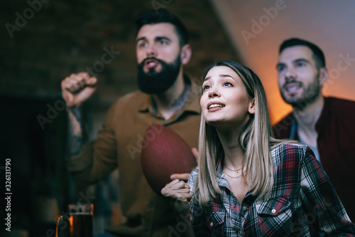 Young woman and her friends watching rugby match on TV at home.