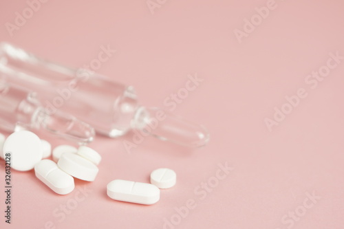 White medical pills and medical preparations in with bottles, glass ampoues, pink background. Closeup photo of medical preparations with copy spaes.