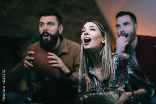 Group of friends shouting while watching rugby match on TV.