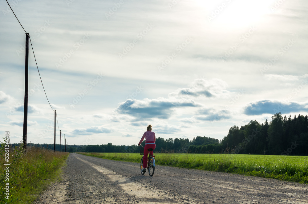 Obraz premium Woman cycling on a countryside road in summer. Photo taken in Lokuta, Turi, in Jarva County, Estonia