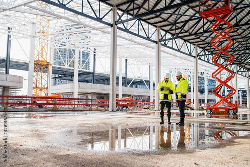 Men engineers standing outdoors on construction site, using tablet.