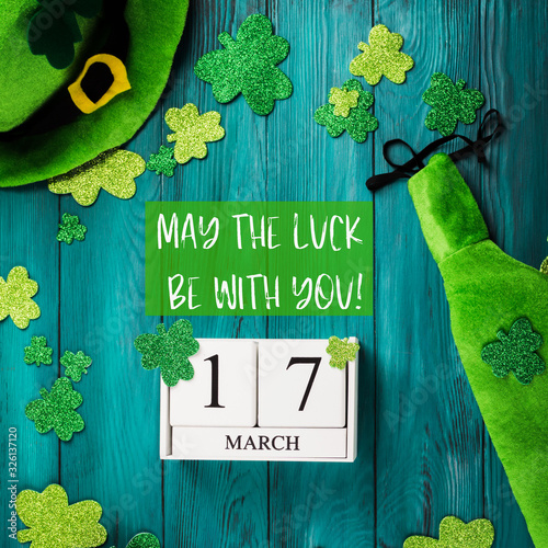 St Patrick Day dark green wooden rustic background with shamrocks and leprechaun costume accessories, date march 17 on vintage wooden calendar. May the luck be with you text quote