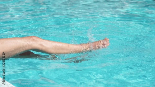 female legs dipping in water in swimming pool. woman splashing water with legs sitting by pool. photo