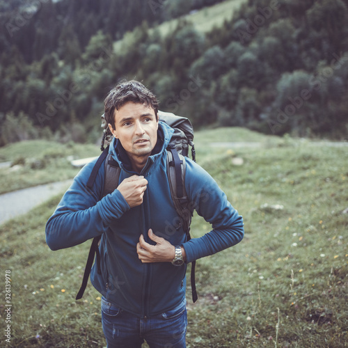 Young man in the mountains during an outdoor advernture/expedition, zipping his jacket as the evening cold is setting in photo
