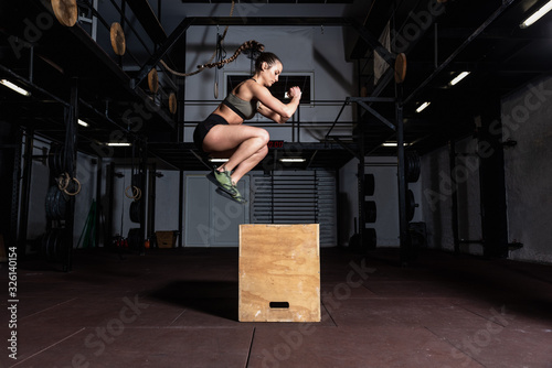 Young strong sweaty fit muscular girl with big muscles doing box jump hardcore crossfit workout training in the gym selective focus motion blur real people exercise