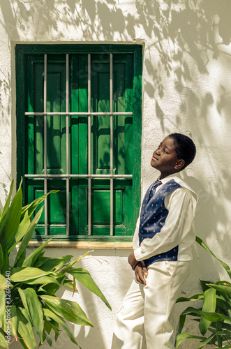 Φωτογραφία Black boy with white shirt and blue tie next to a green window