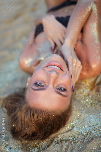 very beautiful woman with incredible blue eyes in black bikini the golden sand. Sensual portrait of amazing girl smiles. Tan beach vacation spa. Sexy model portrait close-up. Glamor sparkles on body