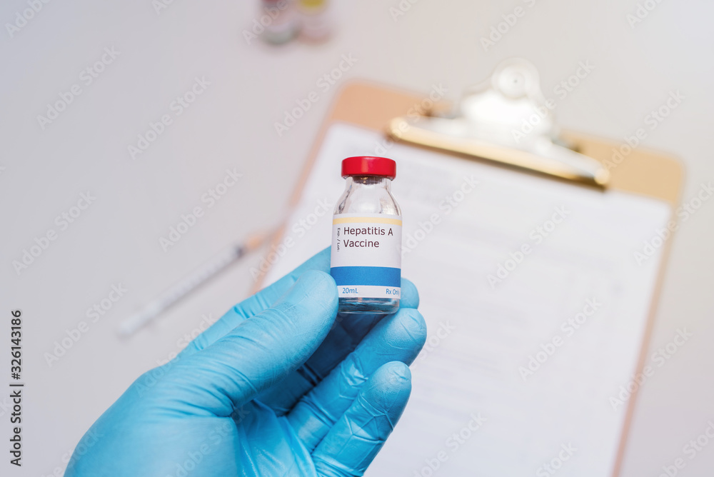 hepatitis A vaccination concept with doctor with blue gloves holding vaccine vial with syringe and clipboard with checklist in background