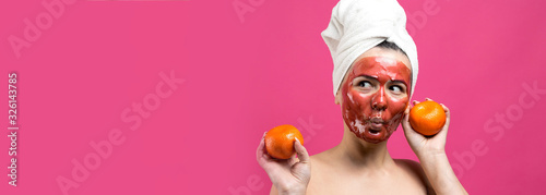 Beauty portrait of woman in white towel on head with red nourishing mask on face. Skincare cleansing eco organic cosmetic spa relax concept. A girl stands with her back holding an orange mandarin. © Mountains Hunter