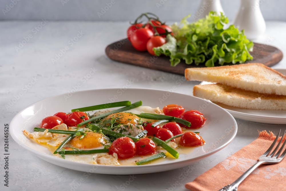 Fried eggs with cherry tomatoes and green onions on a white plate Fried eggs with cherry tomatoes and green onions on a white plate