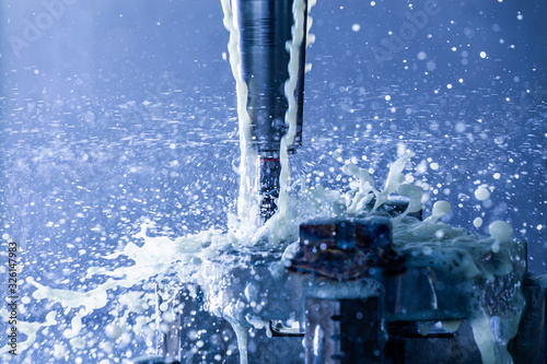 abstract process of vertical cnc steel milling with external water coolant streams and splashes in blue tone photo