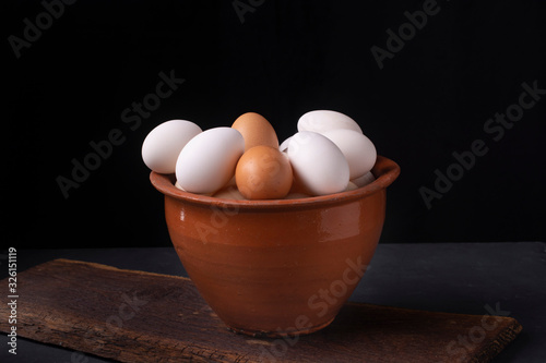 Fresh chicken eggs in a clay pot on a black background.
