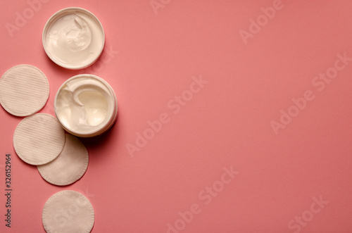 The Bank's with a white cream, napkins for face, the cover is open,on a pink background,cosmetology, beauty and skin care.
